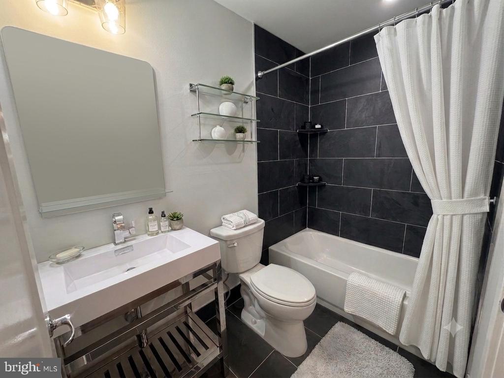 Bathroom with a white vanity and bathtub against dark charcoal tile.