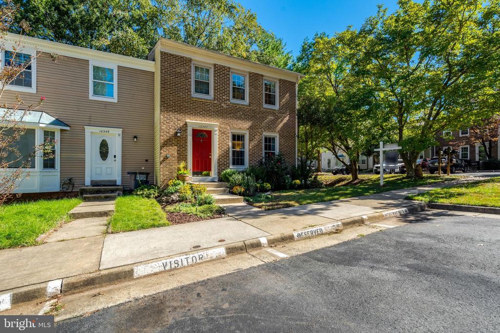 Attached townhome with a red front door, brick facade, and small landscaped garden.