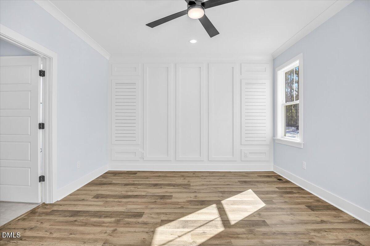 Vacant room with white paneled walls, louvered shutters, and wood-look flooring.