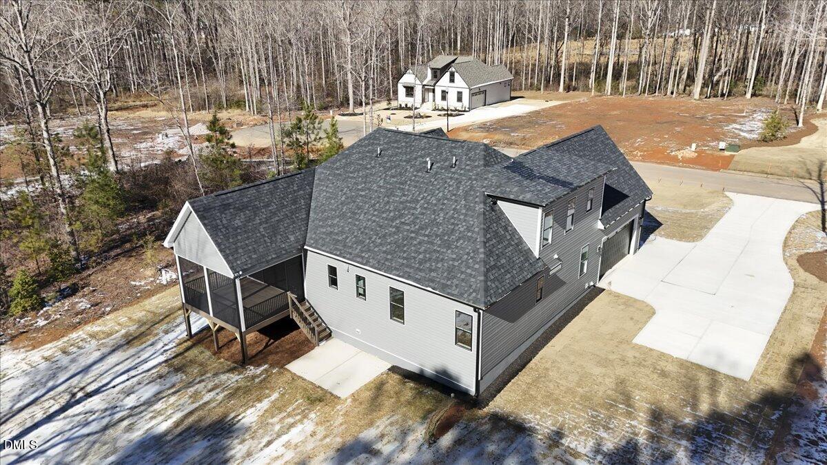 Gray two-story house with a covered porch and broad driveway, viewed from above.