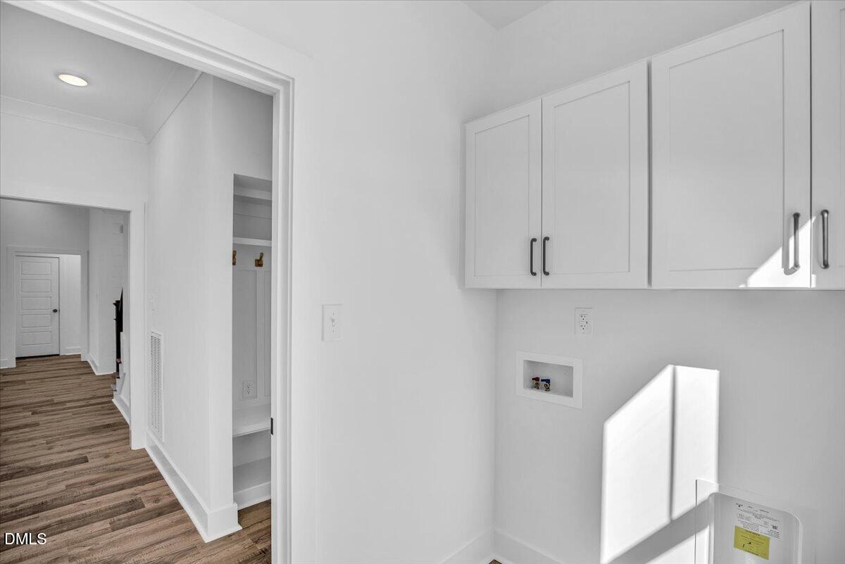 Laundry room with white cabinets and washer hookups beside a wood-look hallway.