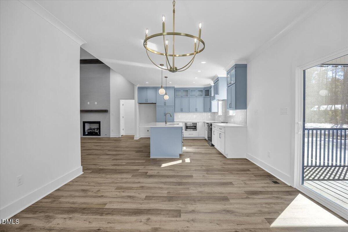 Open kitchen with blue-gray cabinets and island, wood-look floors, fireplace, and glass doors to a deck.