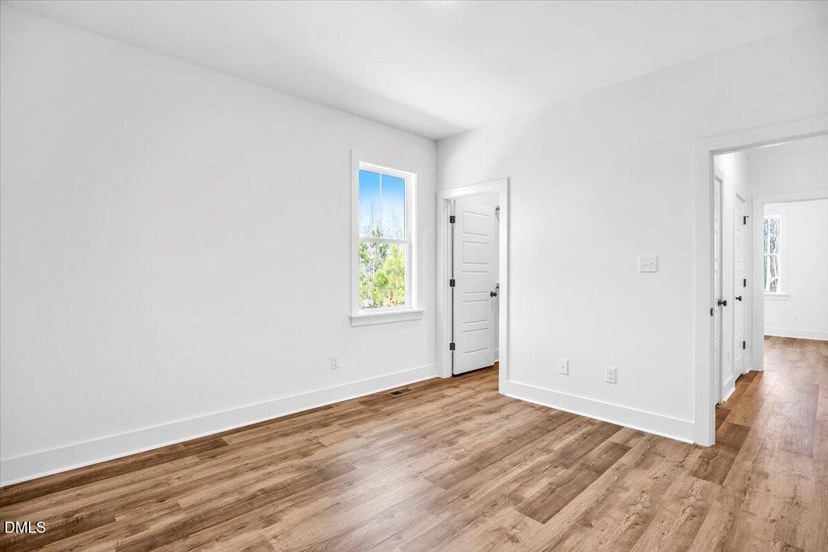Vacant room with warm wood-look flooring, a window, and doorways to adjoining rooms.