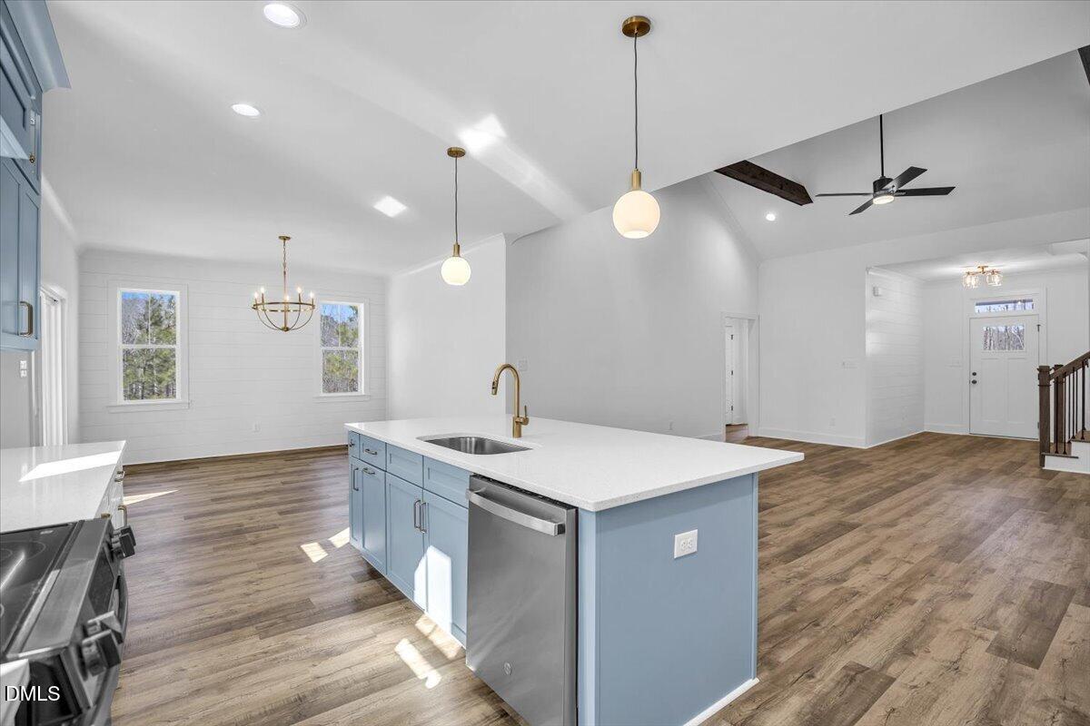 Kitchen with blue cabinets, a large white-topped island, stainless dishwasher, and open living area.