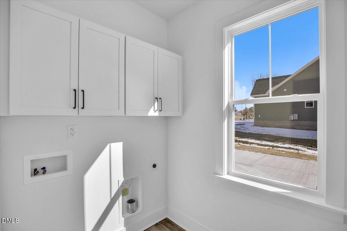Vacant laundry room with white cabinets, washer hookups, and a large window.