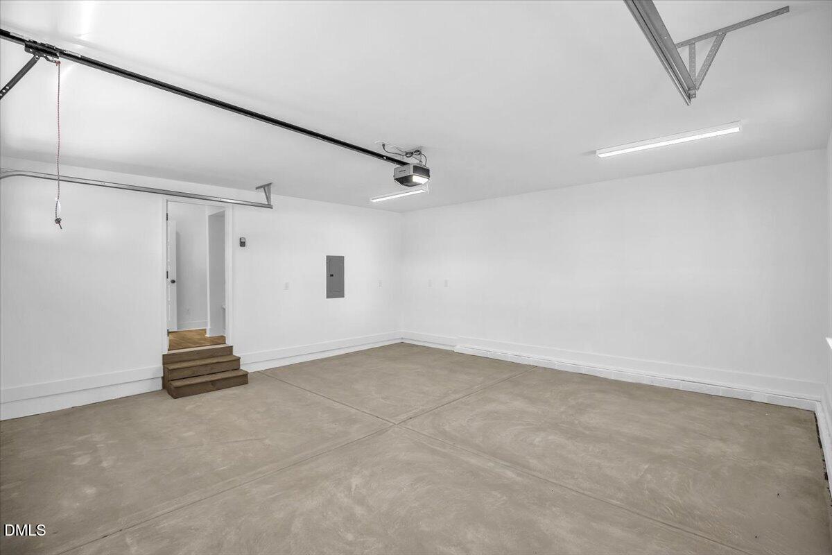 Vacant garage with a broad concrete floor, overhead door tracks, and steps to an interior doorway.
