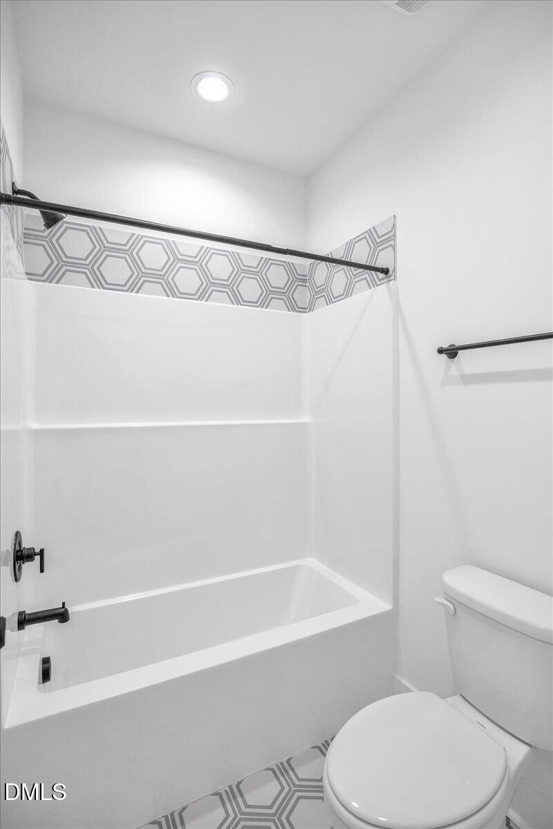 Bathroom with a tub-shower, toilet, and geometric hexagon-patterned accent band and floor tile.