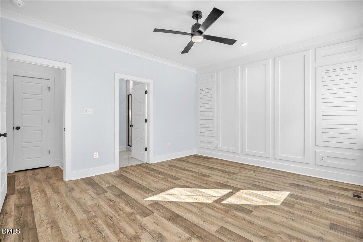 Empty bedroom with white paneled walls, louvered closet doors, wood-look flooring, and a black ceiling fan.