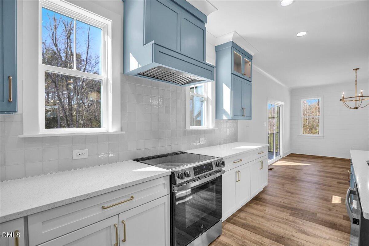 Kitchen with blue cabinets, white counters, stainless steel range, glossy tile backsplash, and wood floors.
