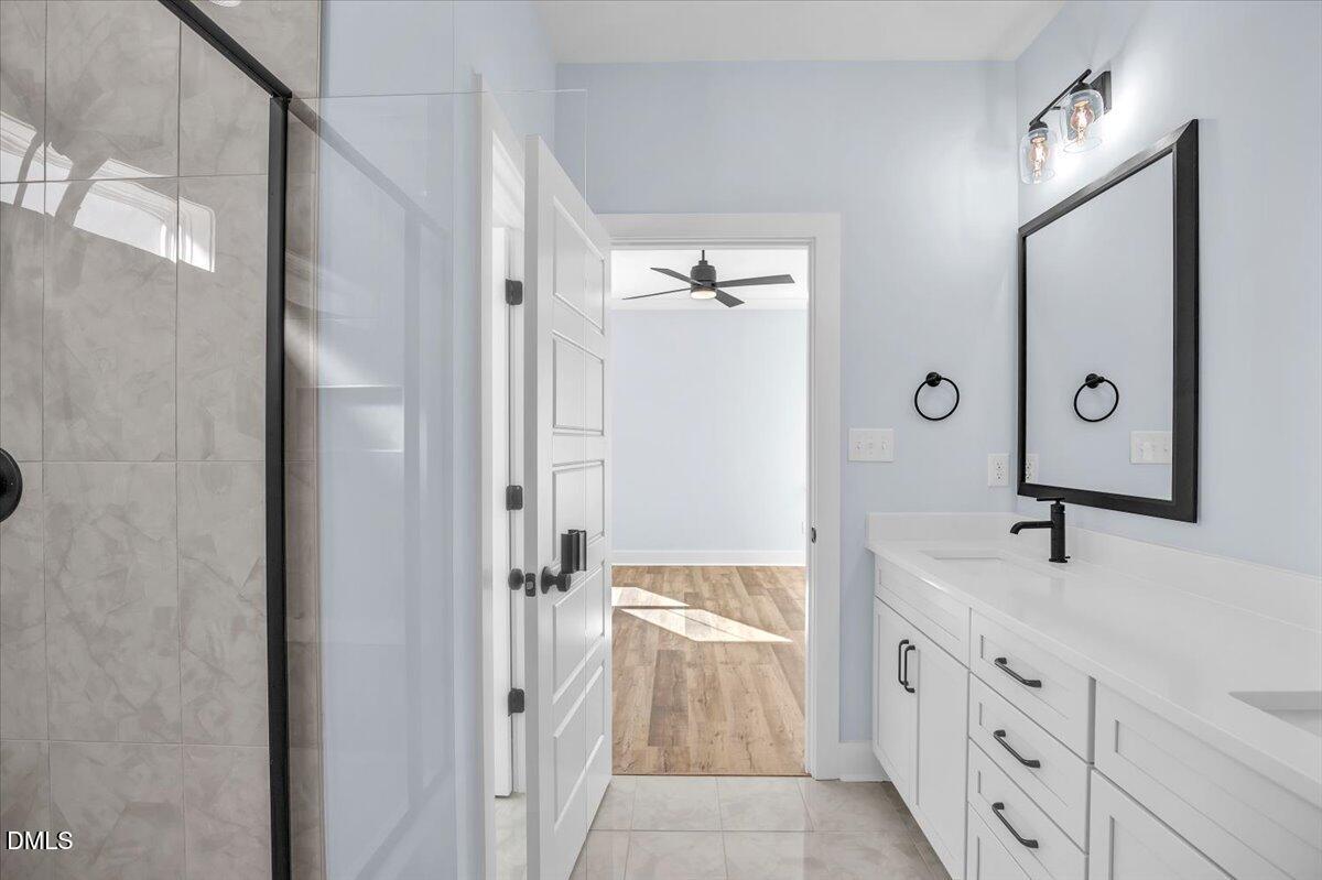 Bathroom with a tiled glass shower and long white vanity with black fixtures.