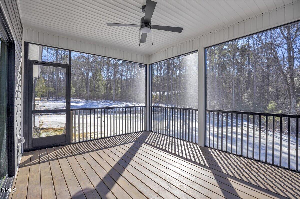 Screened porch with a ceiling fan and black railings overlooking snowy woods.