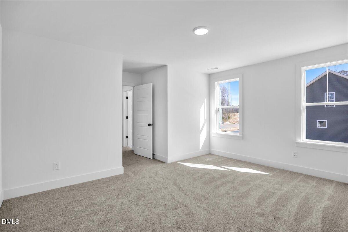 Vacant bedroom with beige carpet, two windows, and an open door.