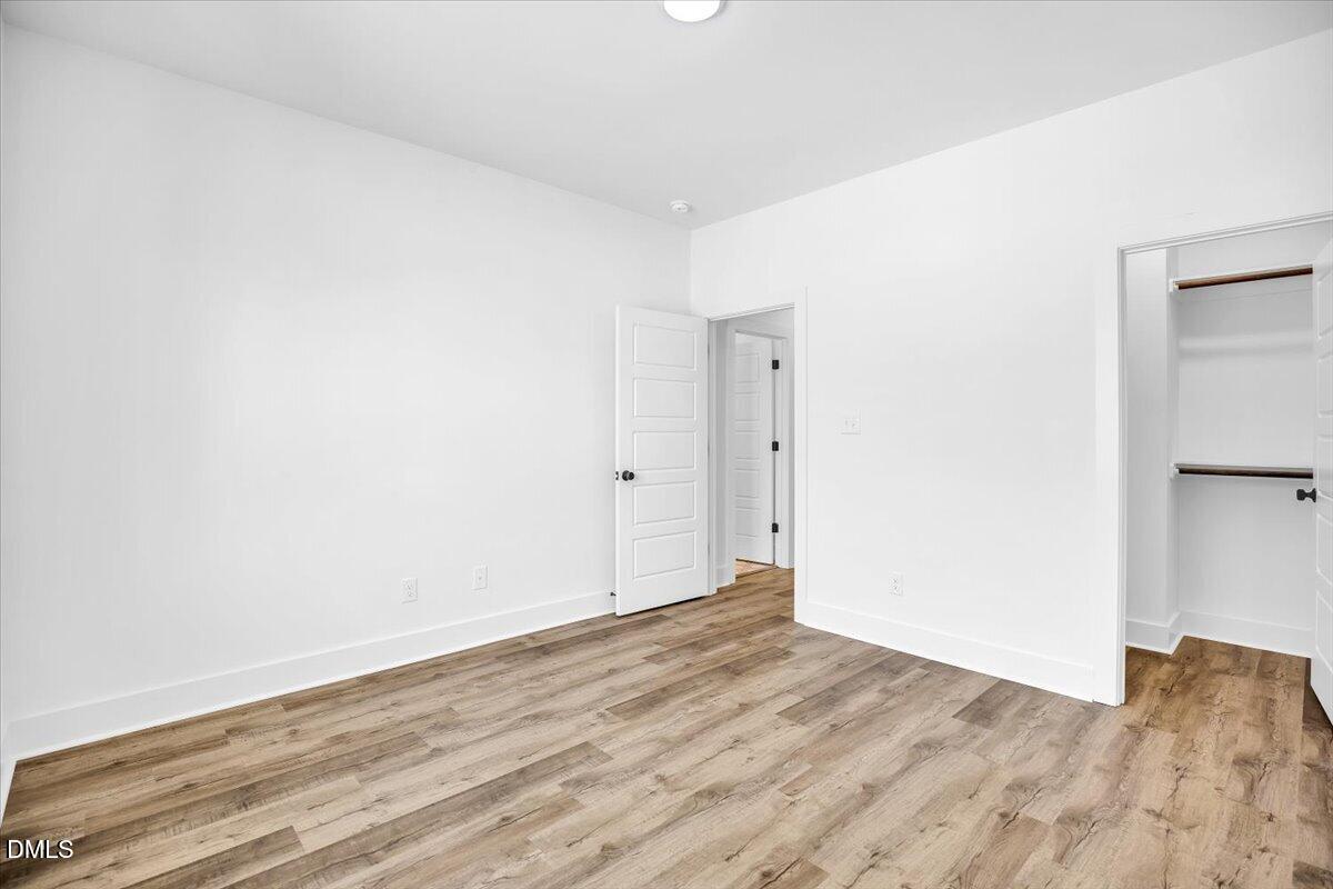 Empty bedroom with wood-look flooring, an open closet, and an open door to the hallway.