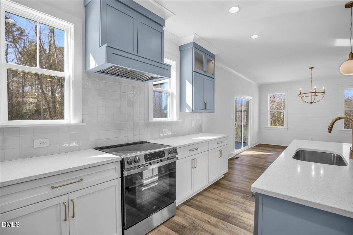 Bright kitchen with blue-gray cabinetry, stainless steel range, tile backsplash, and a large island sink.