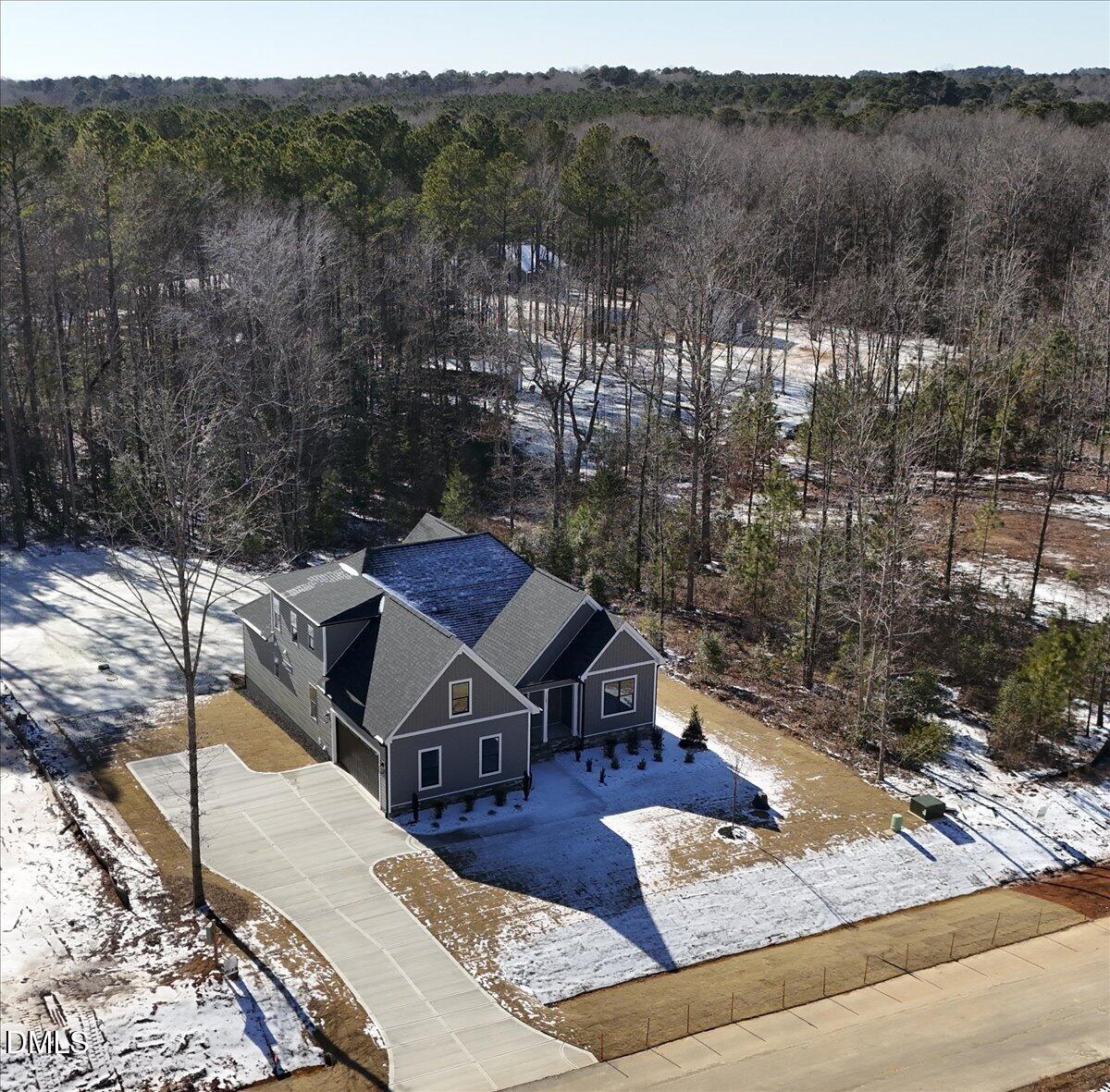 Gray multi-gabled house with a long driveway in a snowy, wooded setting.