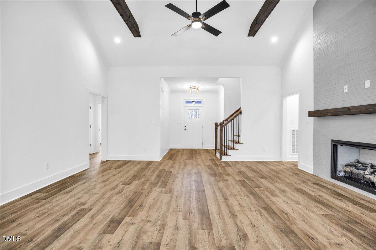 Vacant living room with wood-look floors, exposed ceiling beams, and a white brick fireplace.