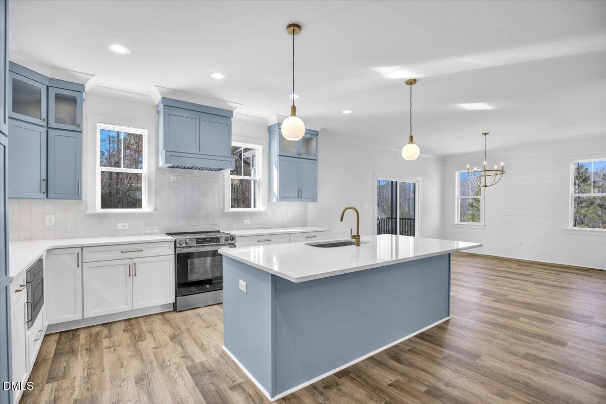 Open kitchen with blue cabinetry, a large island, stainless steel range, and adjoining dining area.