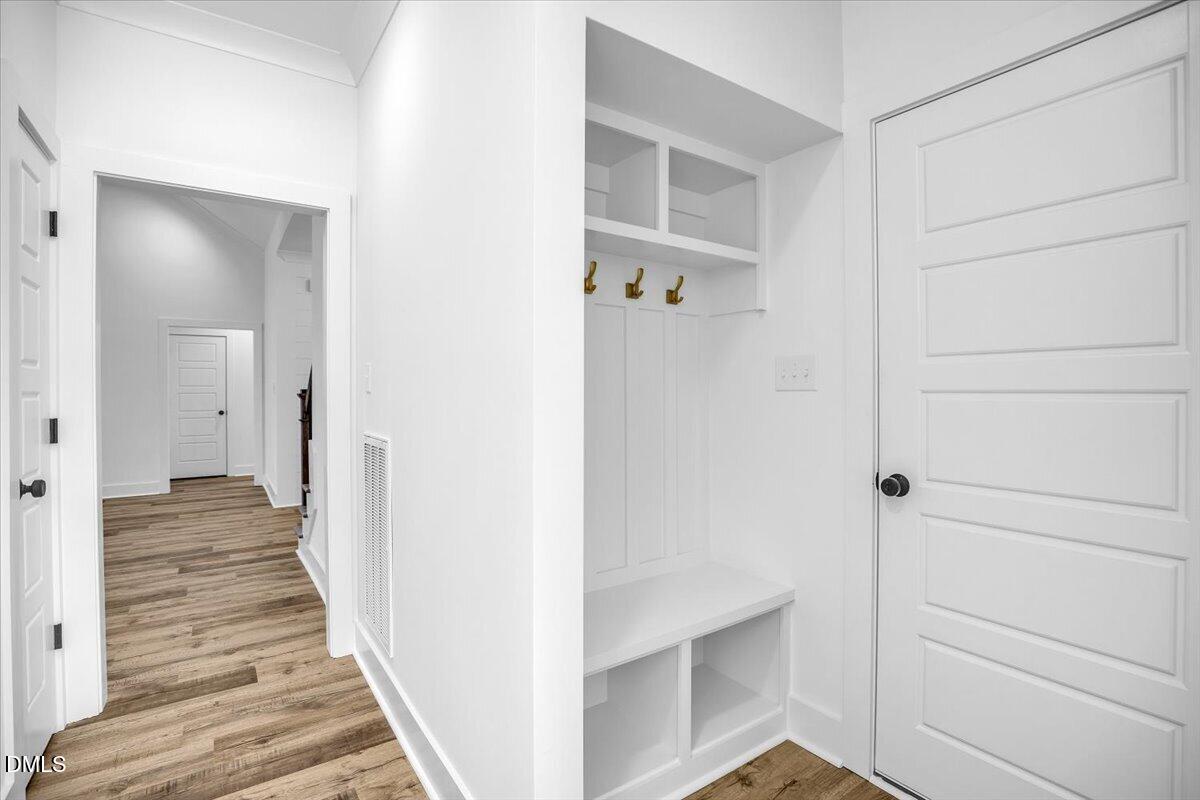 Entryway with a built-in white bench, open cubbies, brass hooks, and wood-look flooring.