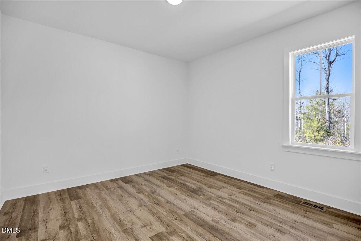 Empty room with wood-look flooring and a large window overlooking trees.