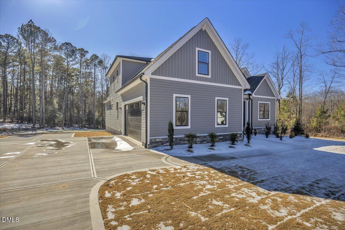Gray two-story home with white-trimmed gables, attached garage, broad driveway, and snow-dusted lawn.