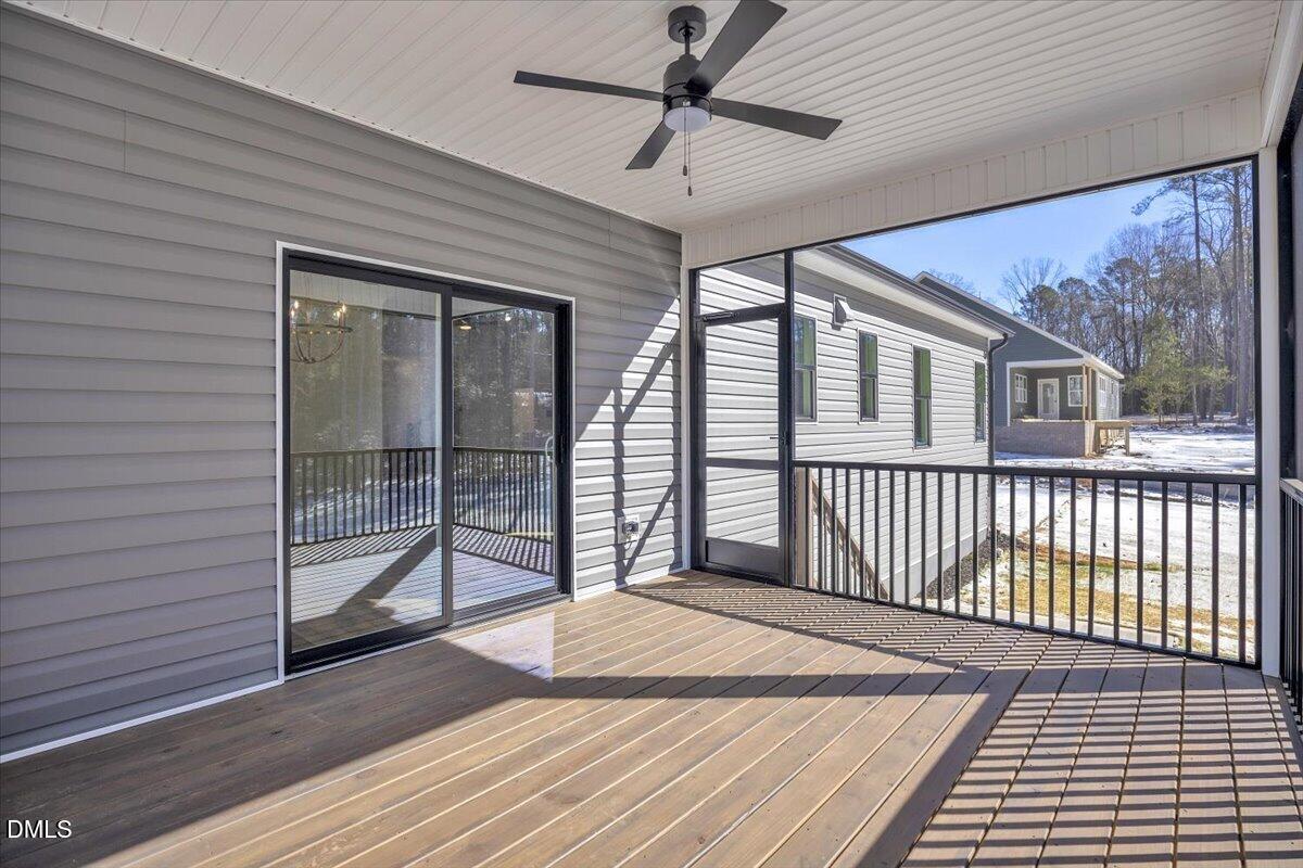 Covered back porch with a wooden deck, black railings, and a ceiling fan overlooking a snowy yard.