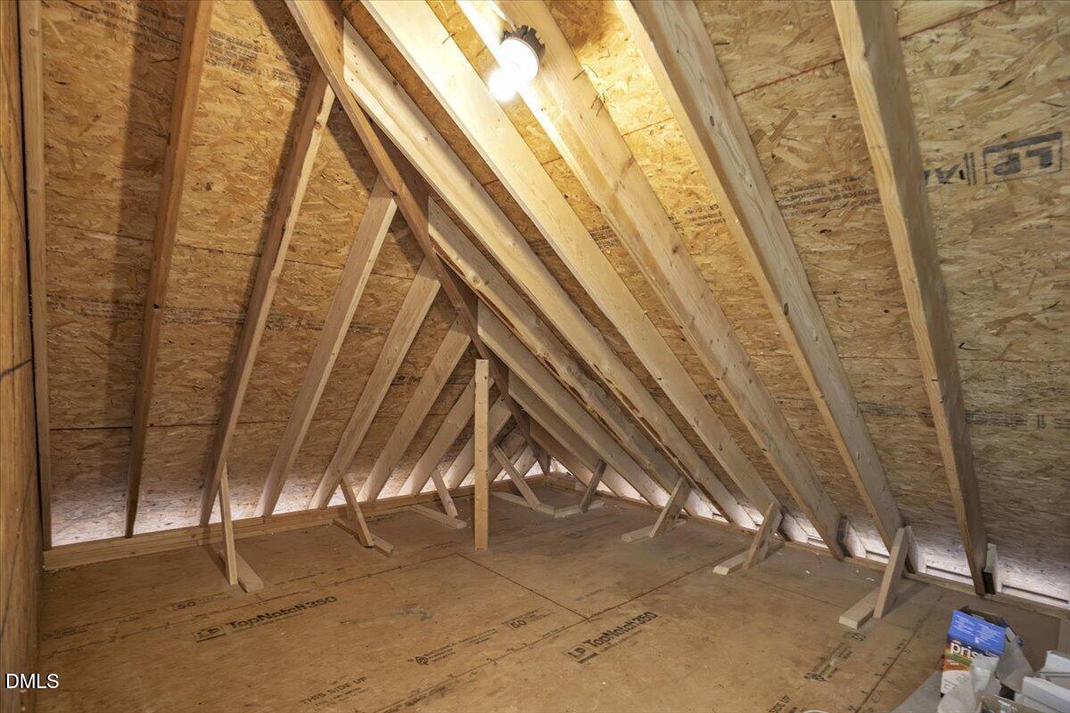 Unfinished attic with exposed wooden trusses, OSB sheathing, and plywood flooring.