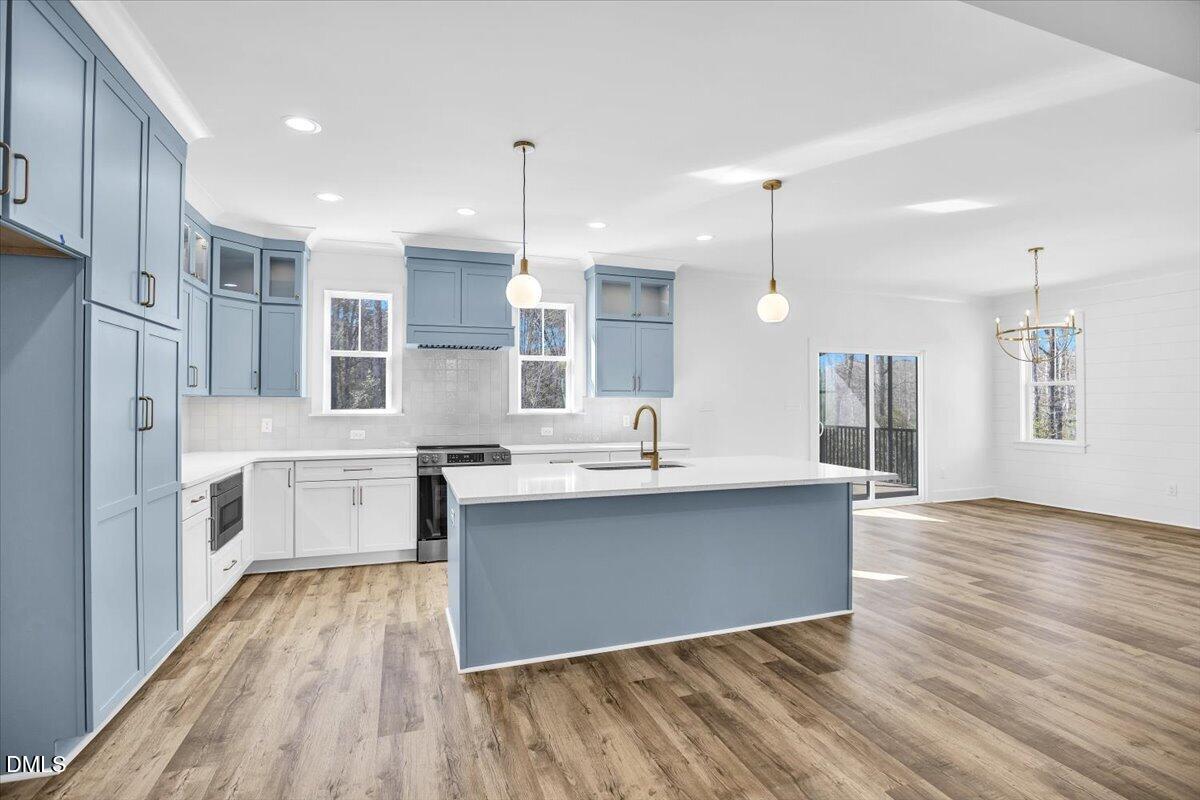 Kitchen with blue-gray cabinets, a large island, brass faucet, and wood-look flooring.
