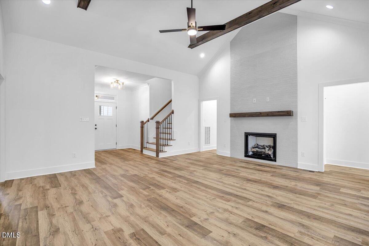 Vacant living room with vaulted ceiling, exposed beam, wood-look floors, and a tiled fireplace.