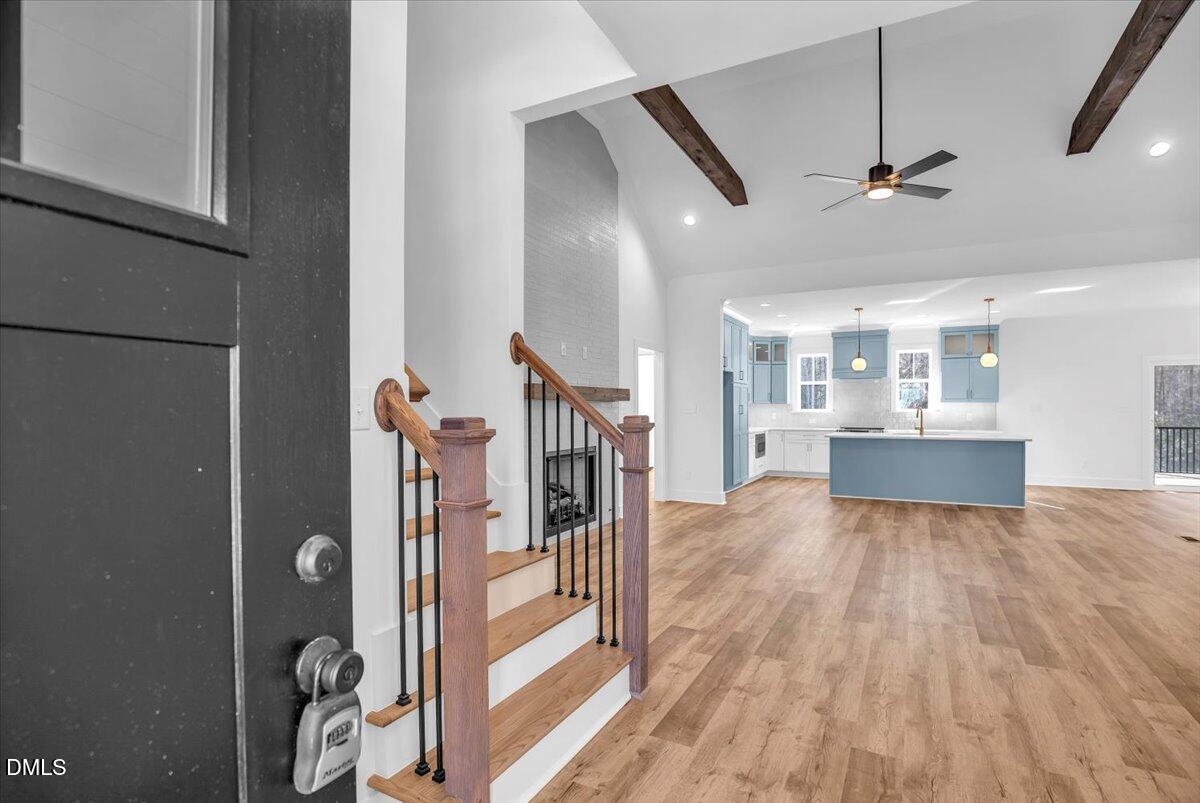 Open-plan entry and kitchen with a wood staircase, vaulted ceiling, and blue island.