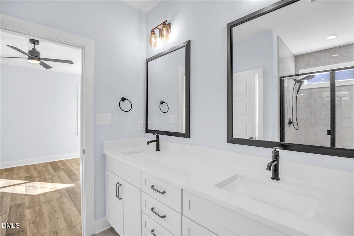 Bathroom with a long white double vanity, black faucets, framed mirrors, and a tiled walk-in shower.