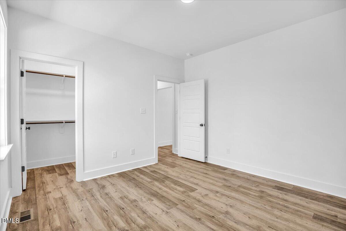Empty bedroom with wood-look flooring, an open double-rod closet, and an open doorway.