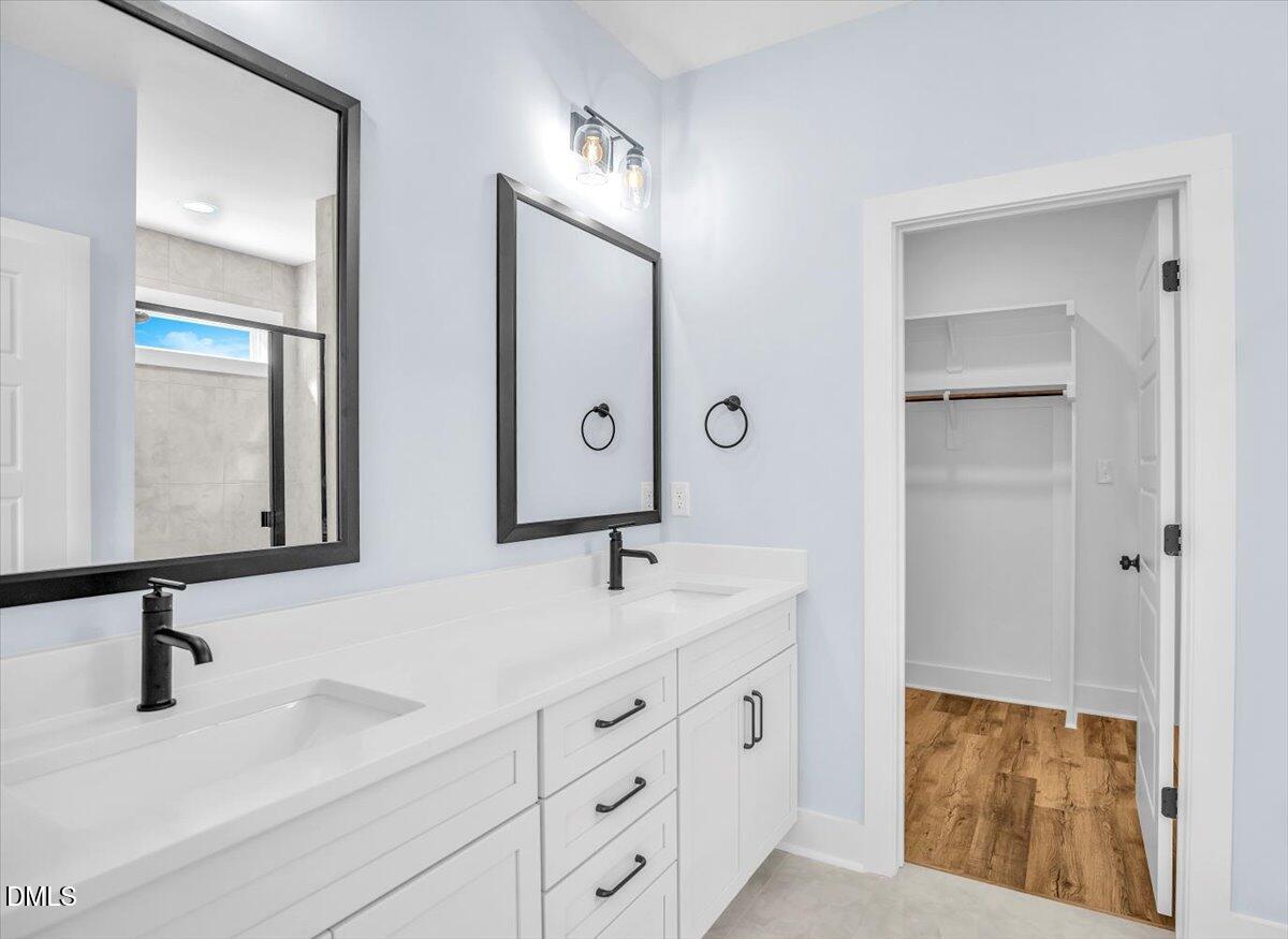 Bathroom with a white double-sink vanity and an open doorway to a walk-in closet.
