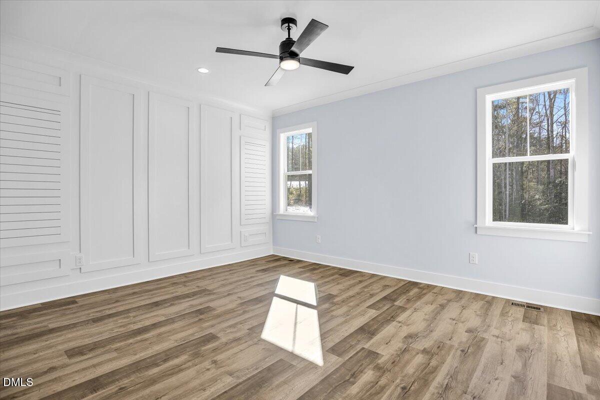 Empty room with paneled walls, wood-look flooring, a ceiling fan, and two windows.