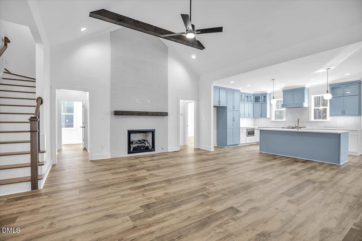 Open living room and kitchen with a tall fireplace wall, staircase, and blue cabinets and island.