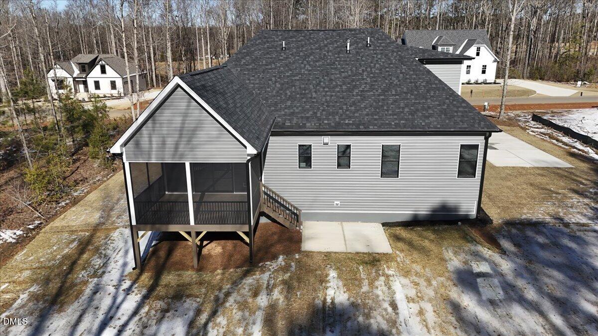 Rear aerial view of a gray-sided home with a raised screened porch and wooded lot.