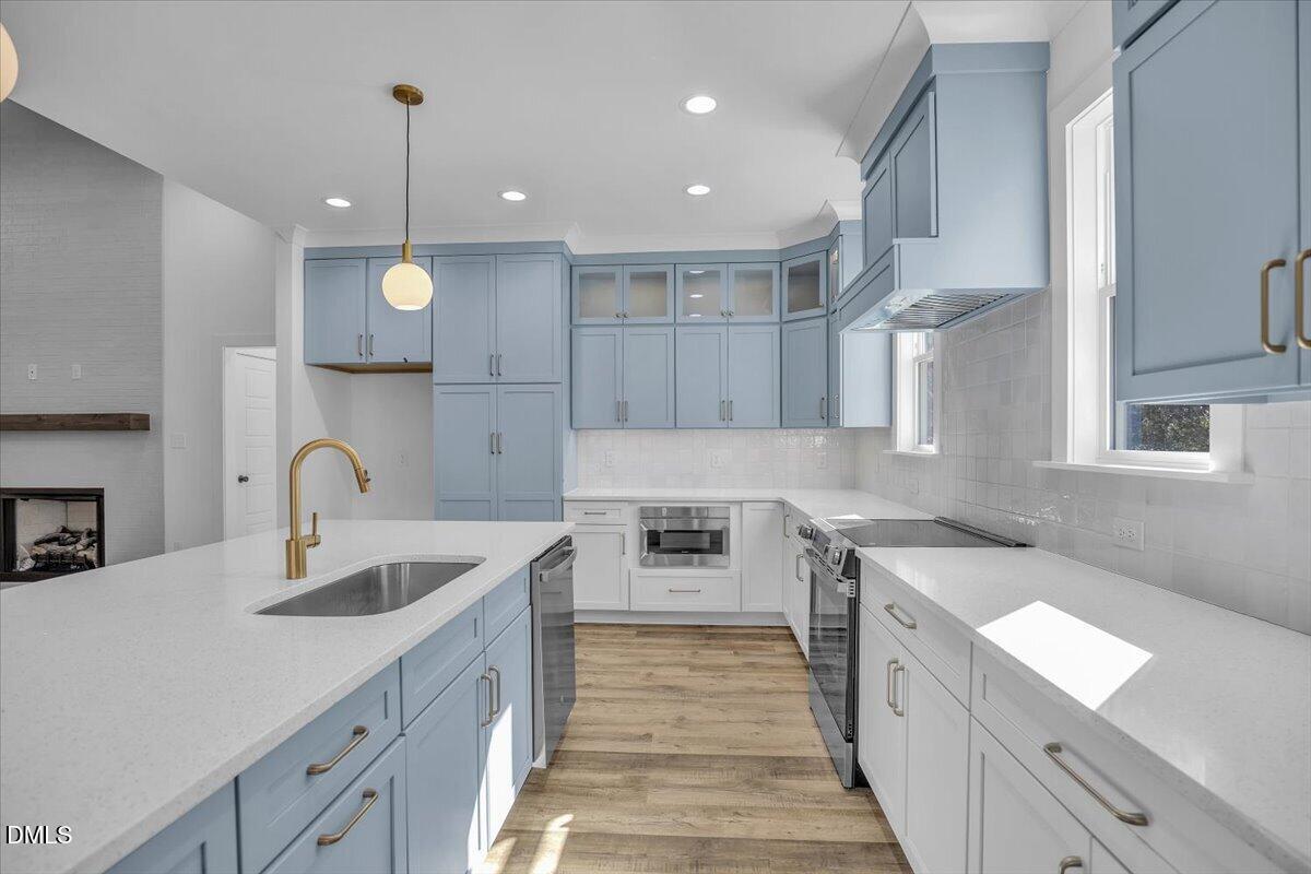 Kitchen with pale blue cabinetry, a white island, brass faucet, stainless appliances, and wood-look floors.