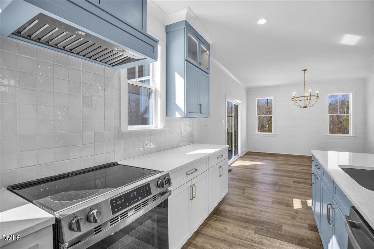 Kitchen with blue and white cabinets, stainless steel range, glossy tile backsplash, and adjoining dining area.