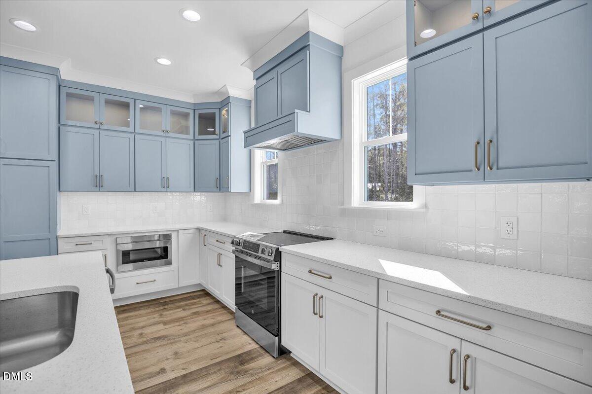 Kitchen with blue cabinets, white tile backsplash, stainless steel appliances, and wood-look flooring.