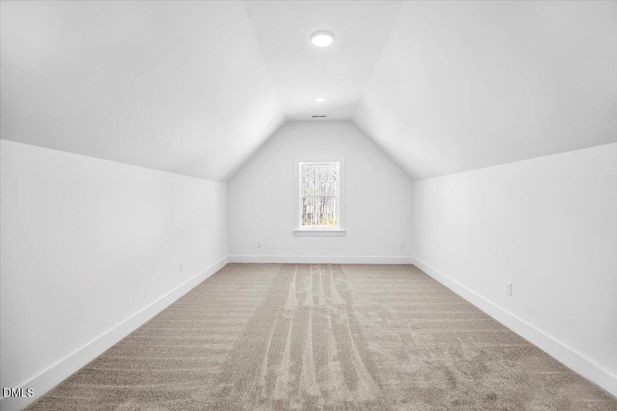 Empty carpeted room with a high sloped ceiling and a window overlooking trees.
