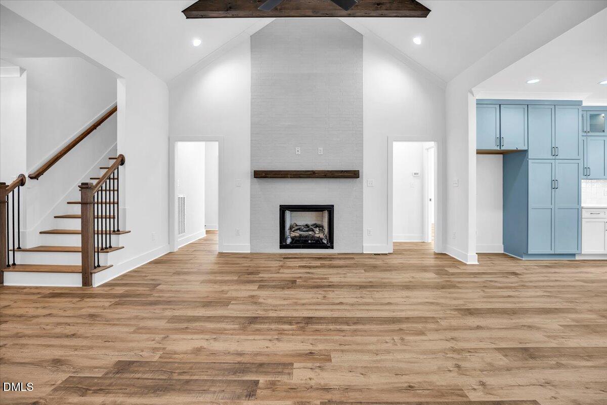 Open living area with a tall white brick fireplace, wood staircase, and blue kitchen cabinets.