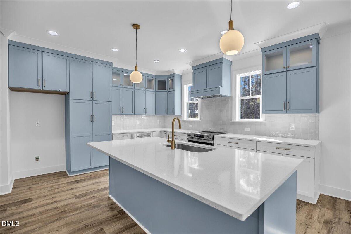 Blue-and-white kitchen with a large island, brass fixtures, and wood-look flooring.