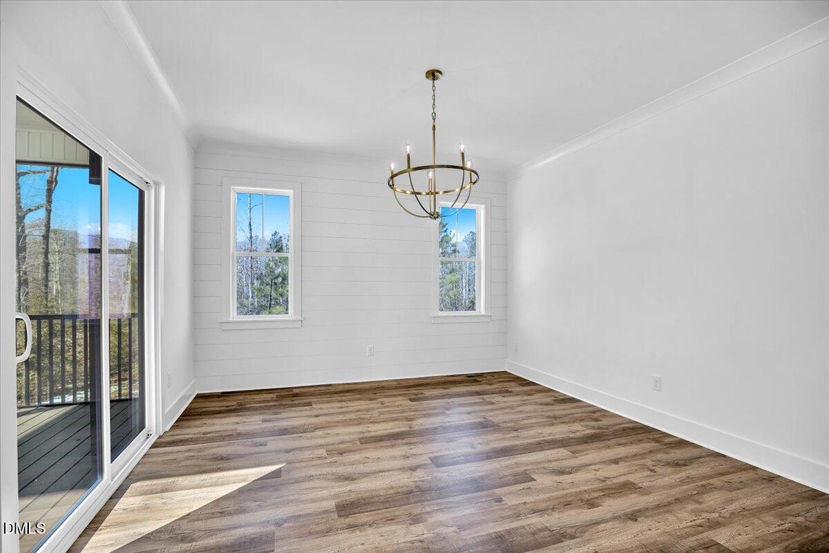 Vacant dining room with white paneling, wood-look floors, and a brass chandelier beside a sliding glass door.