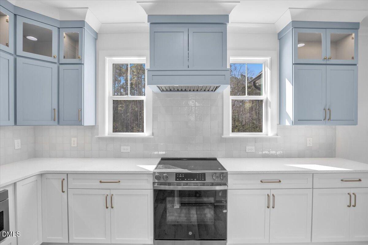 Kitchen with pale blue cabinets, a stainless steel range, and windows overlooking trees.