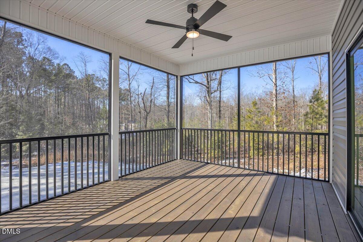 Screened porch with a ceiling fan and wooded views beyond the black railings.