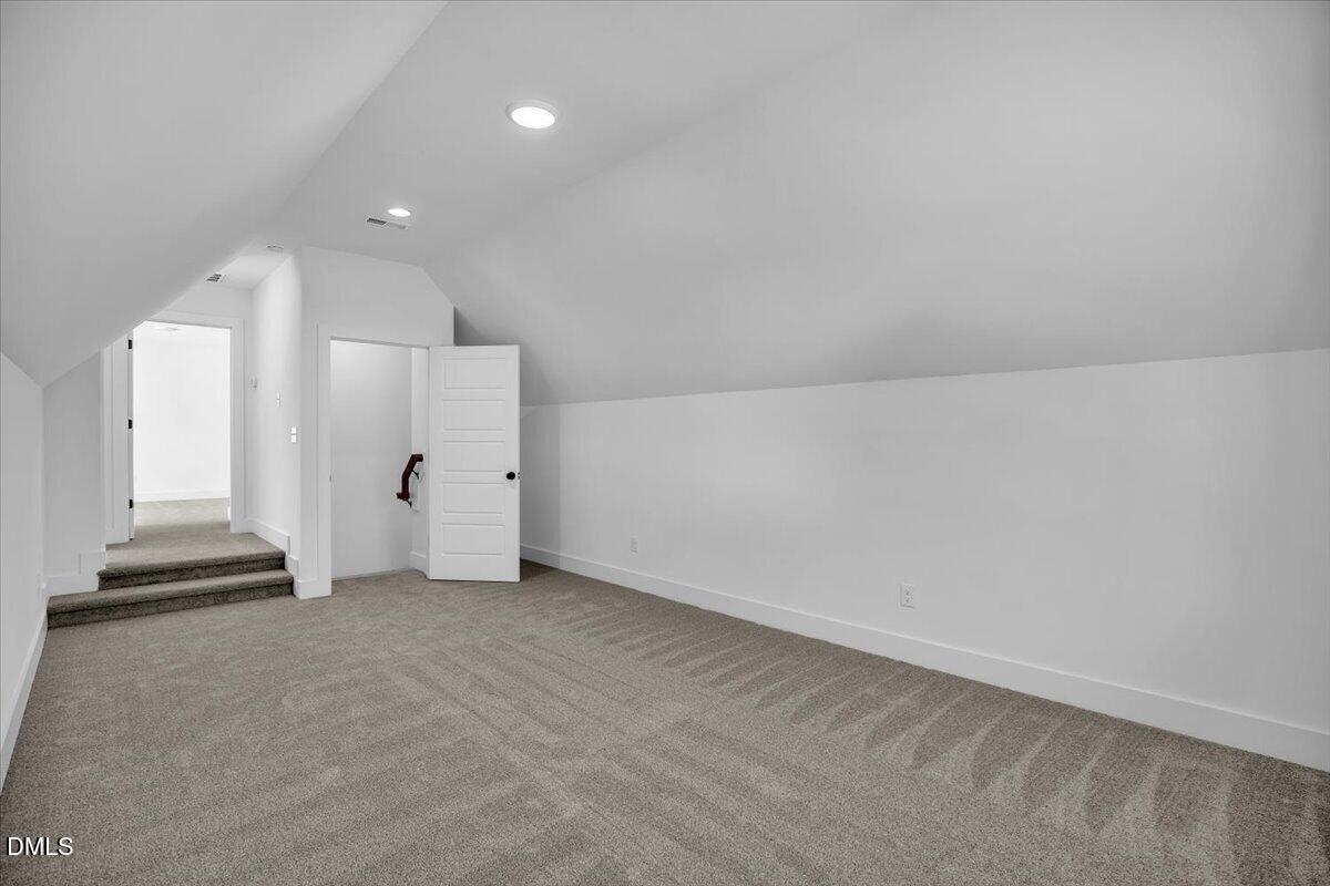 Empty finished attic room with gray carpet, sloped ceilings, and recessed lights.