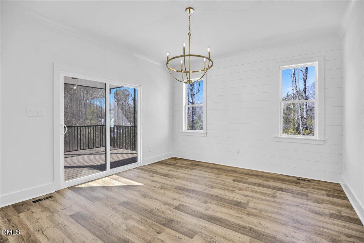Empty room with a brass chandelier, wood-look floors, and sliding doors to a deck.