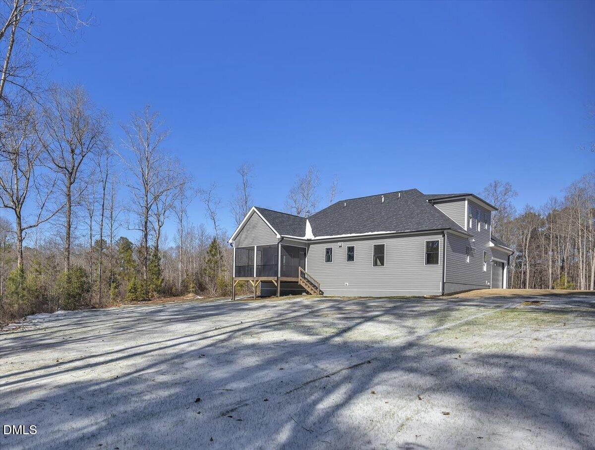 Gray two-story home with a screened porch and gravel driveway, surrounded by leafless trees.