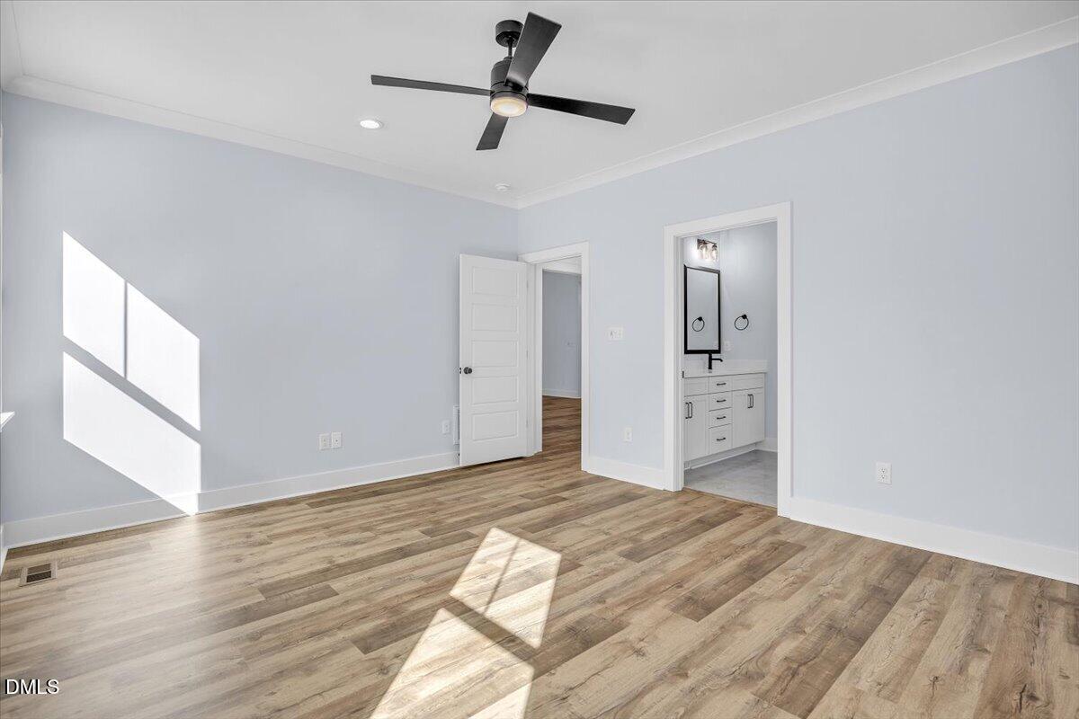 Empty bedroom with wood-look flooring, a black ceiling fan, and an adjoining bathroom.