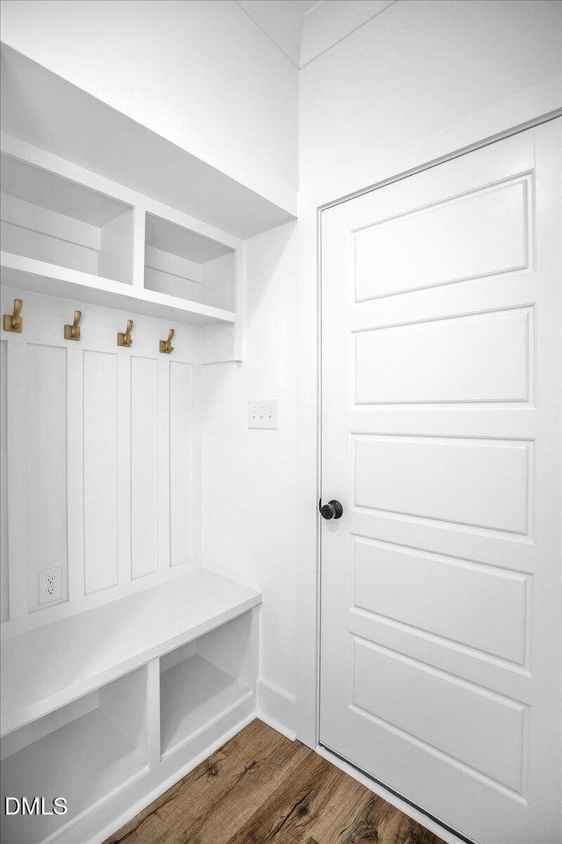 Mudroom with a built-in white bench, open cubbies, brass hooks, and paneled door.