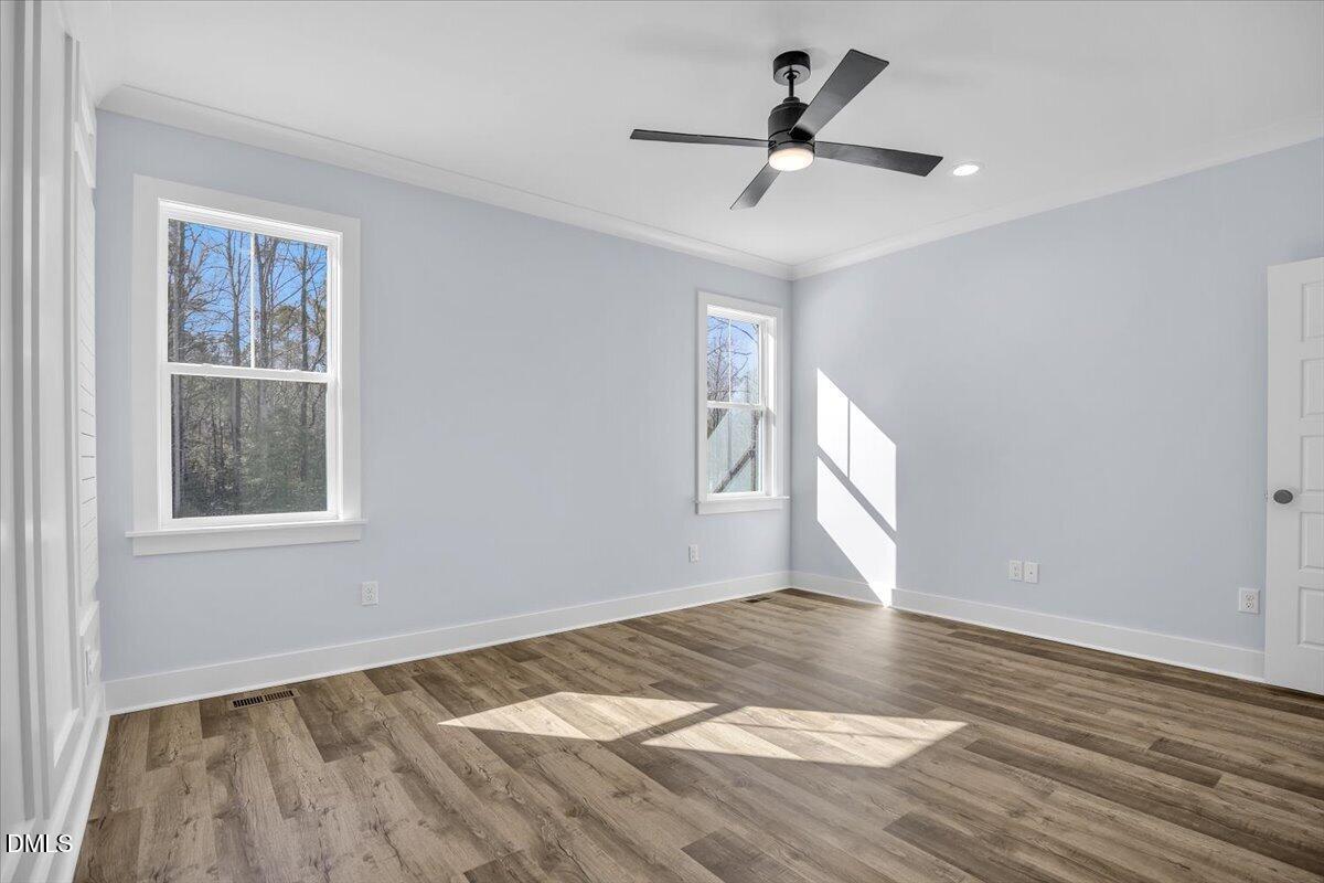 Empty bedroom with gray walls, two windows, wood-look floors, and a black ceiling fan.